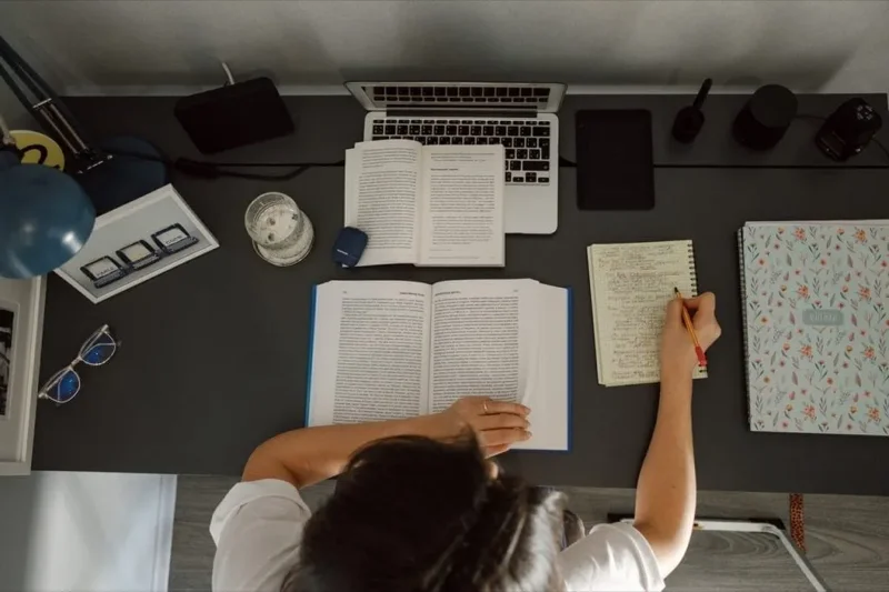 12 informações relevantes para o seu portfolio: mulher trabalhando em mesa com diversos livros, caderno e notebook.