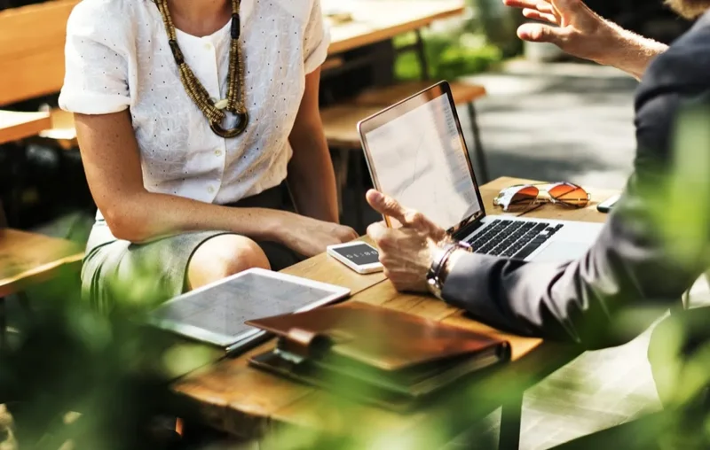 5 diferenças entre portfolios eficientes e portfolios ruins: duas pessoas sentadas, conversando ao redor de uma mesa com notebook e cadernos em cima.