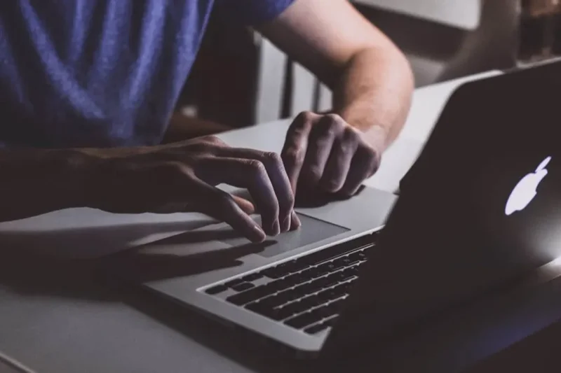 Pessoa trabalhando em um notebook, com dedos da mão direita mexendo no trackpad.