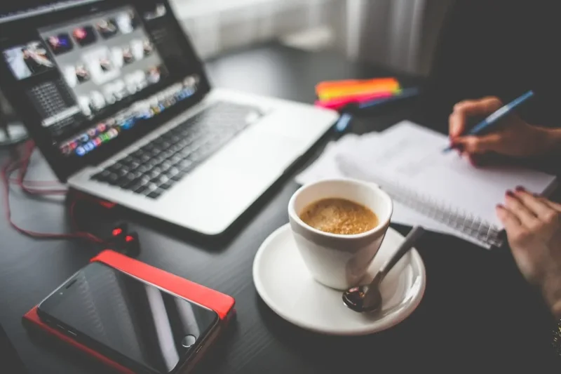 Portfolio: imagem de alguém trabalhando em uma mesa com laptop, celular, caderno e um cafezinho.